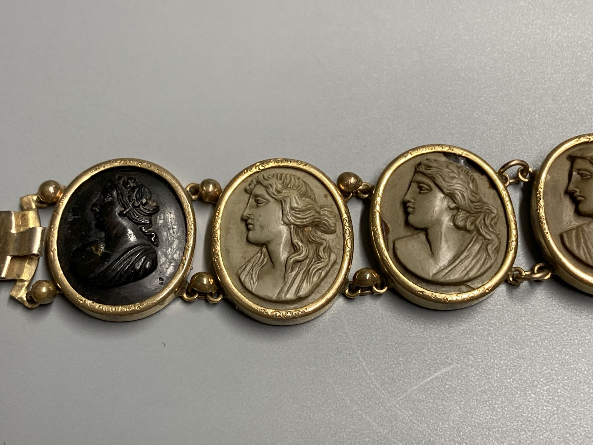 A late Victorian gilt metal bracelet set with seven oval lava plaques carved with busts of ladies, 17cm.